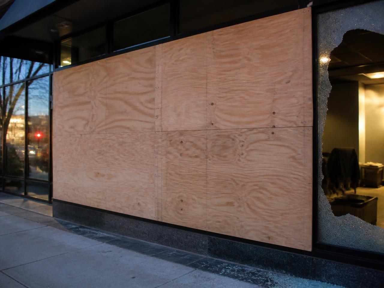 Emergency plywood board-up securing a broken storefront window at night