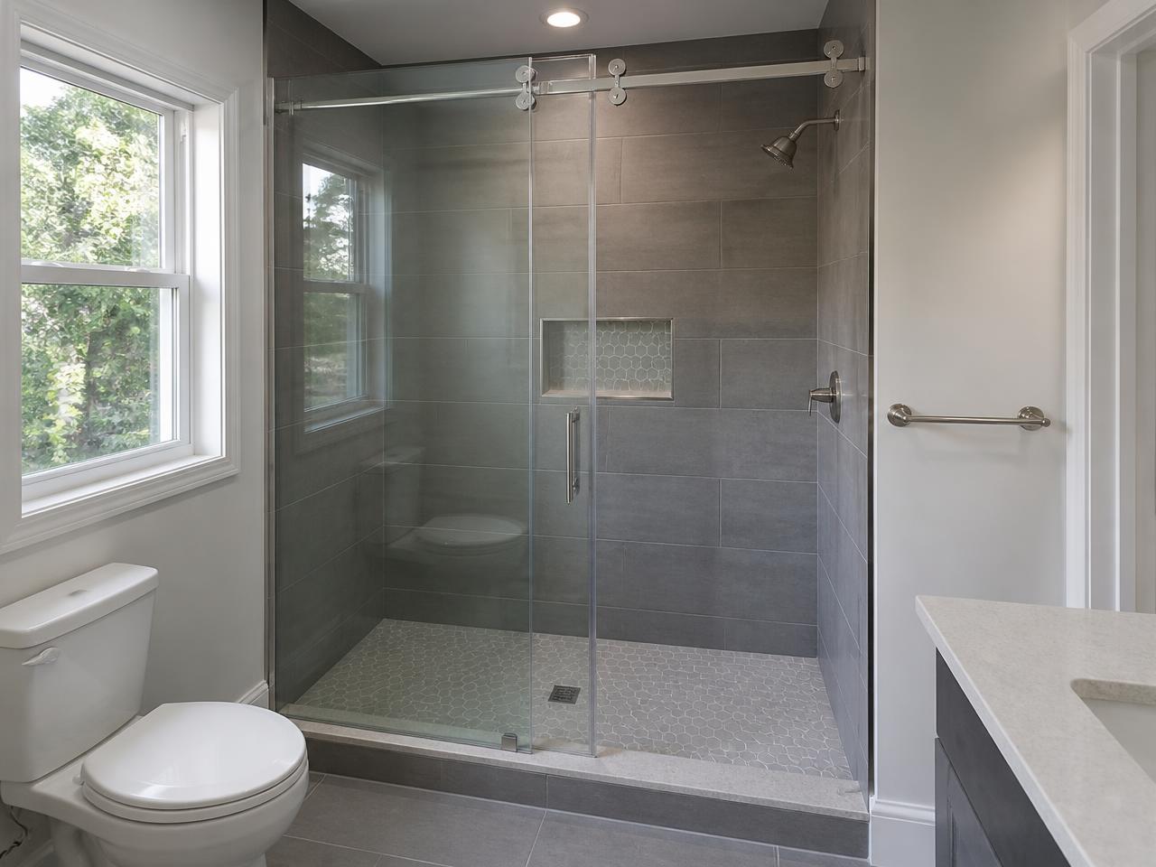 Frameless sliding glass shower door on grey tile with brushed nickel rail hardware